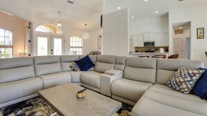 A spacious living room with a large L-shaped sectional sofa, a coffee table, and a kitchen in the background. - Florida Vacation Rental w/ Private Pool & Lanai (North Port)