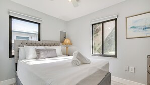 Una cama bien hecha con una toalla enrollada, una lámpara y un cuadro en la pared.