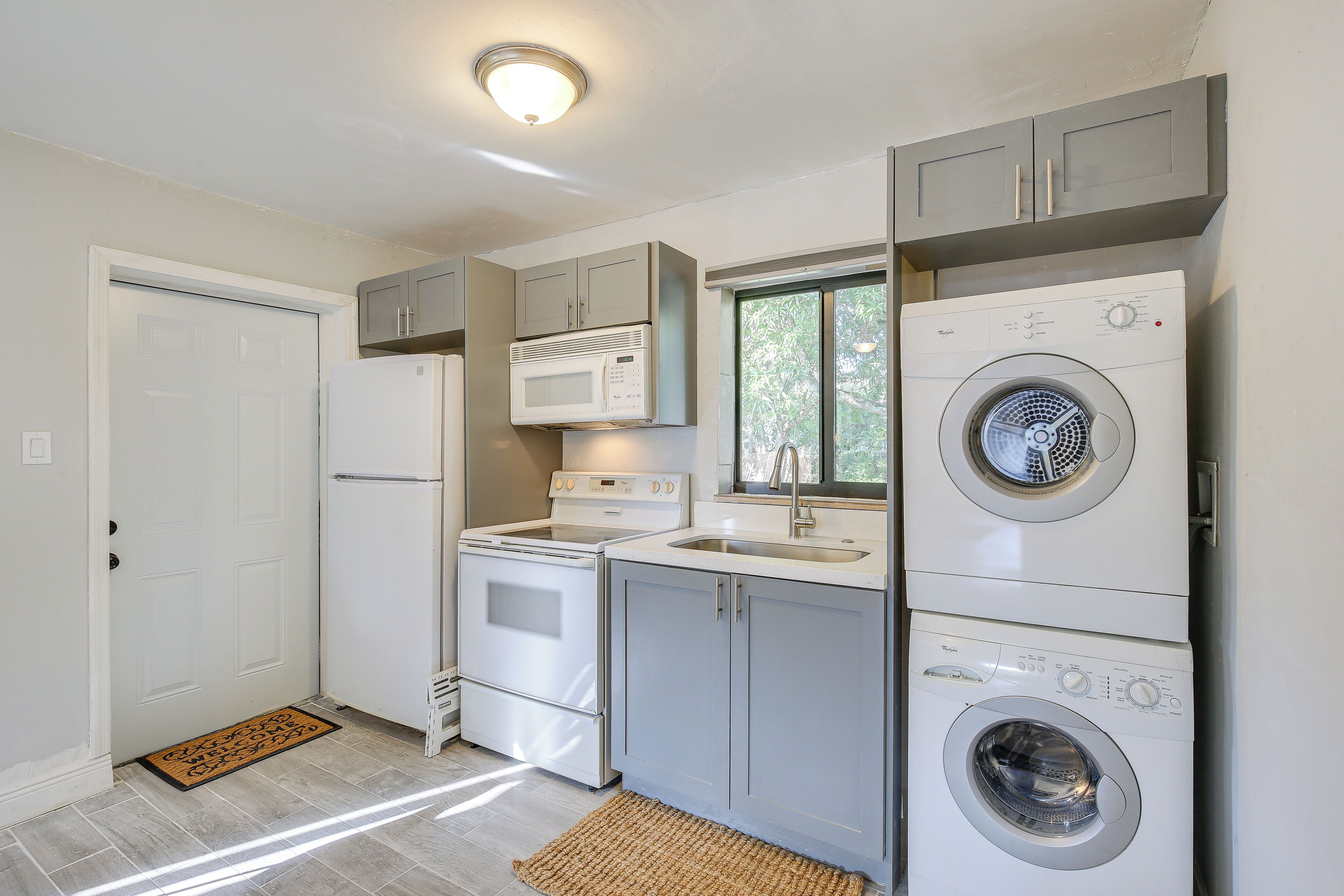 Cocina compacta con refrigerador, microondas, estufa, lavaplatos y lavadora y secadora apiladas.