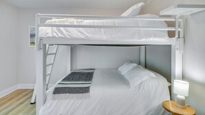A bunk bed with white bedding, a gray and white striped throw blanket, and a bedside lamp on a wooden nightstand. - Florida Getaway w/ Heated Pool, Bar & Fire Table! (Cape Coral)