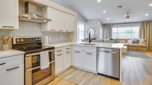 A modern kitchen with white cabinetry, a stainless steel range hood, and a built-in dishwasher. - Florida Getaway w/ Heated Pool, Bar & Fire Table! (Cape Coral)