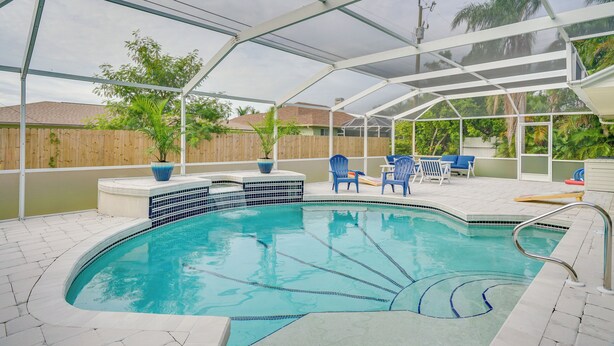 A covered swimming pool with blue chairs and potted plants. - Florida Getaway w/ Heated Pool, Bar & Fire Table! (Cape Coral)