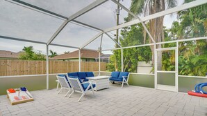 A covered patio area with a white metal frame, blue and white furniture, and a paved floor. - Florida Getaway w/ Heated Pool, Bar & Fire Table! (Cape Coral)