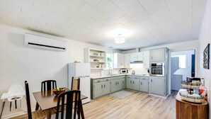 Una cocina moderna con armarios de colores claros, un comedor con mesa y sillas de madera, y un techo blanco con foco empotrado.