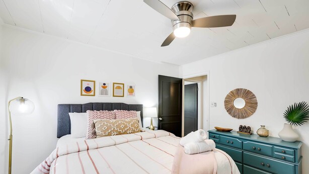 Un dormitorio con cama, cómoda, ventilador de techo y decoración en la pared.