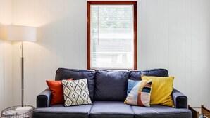 Un sofá gris con cojines estampados, una lámpara de pie y una ventana con persianas.