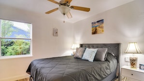 A bedroom with a bed, a ceiling fan, a nightstand, a lamp, and a window with blinds. - Pet-friendly Gulfport Home: Walkable Location! (St. Petersburg)