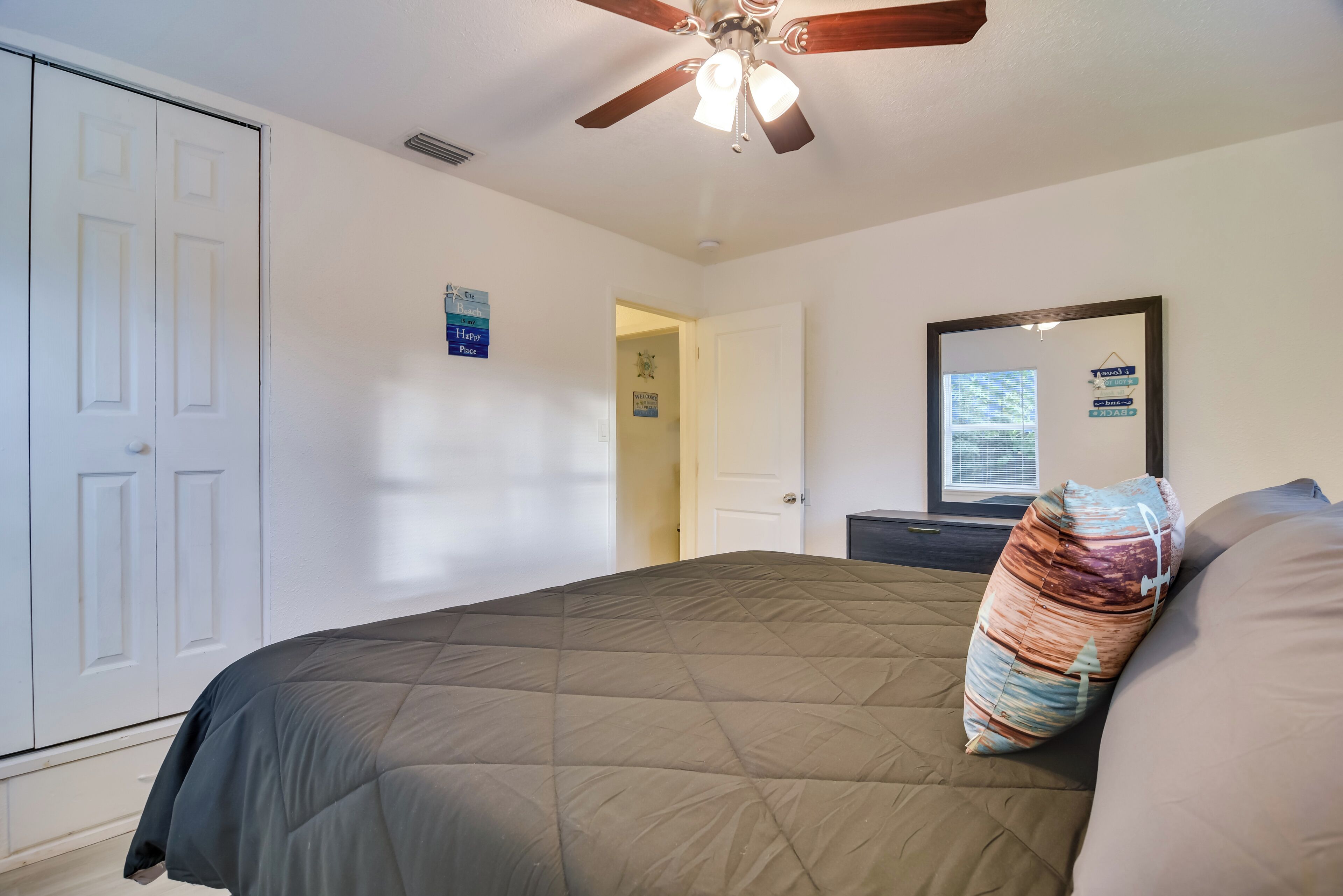 A bedroom with a bed, a ceiling fan, a door, and a wall with a mirror and a sign.
