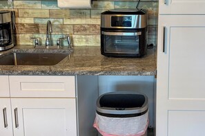 A kitchen with a stainless steel coffee maker, a sink, and a trash bin.