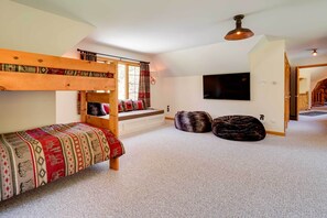 Quarto com beliche, uma janela grande com cortinas, televisão de tela plana e escada para outro andar.