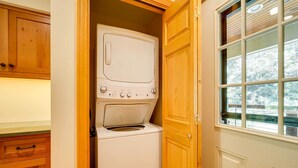 A compact laundry room with a front-loading washer and dryer, wooden cabinetry, and a window with a view of trees. - Winhall Home w/ Deck + Views, 6 Mi to Ski Slopes! (Bondville)