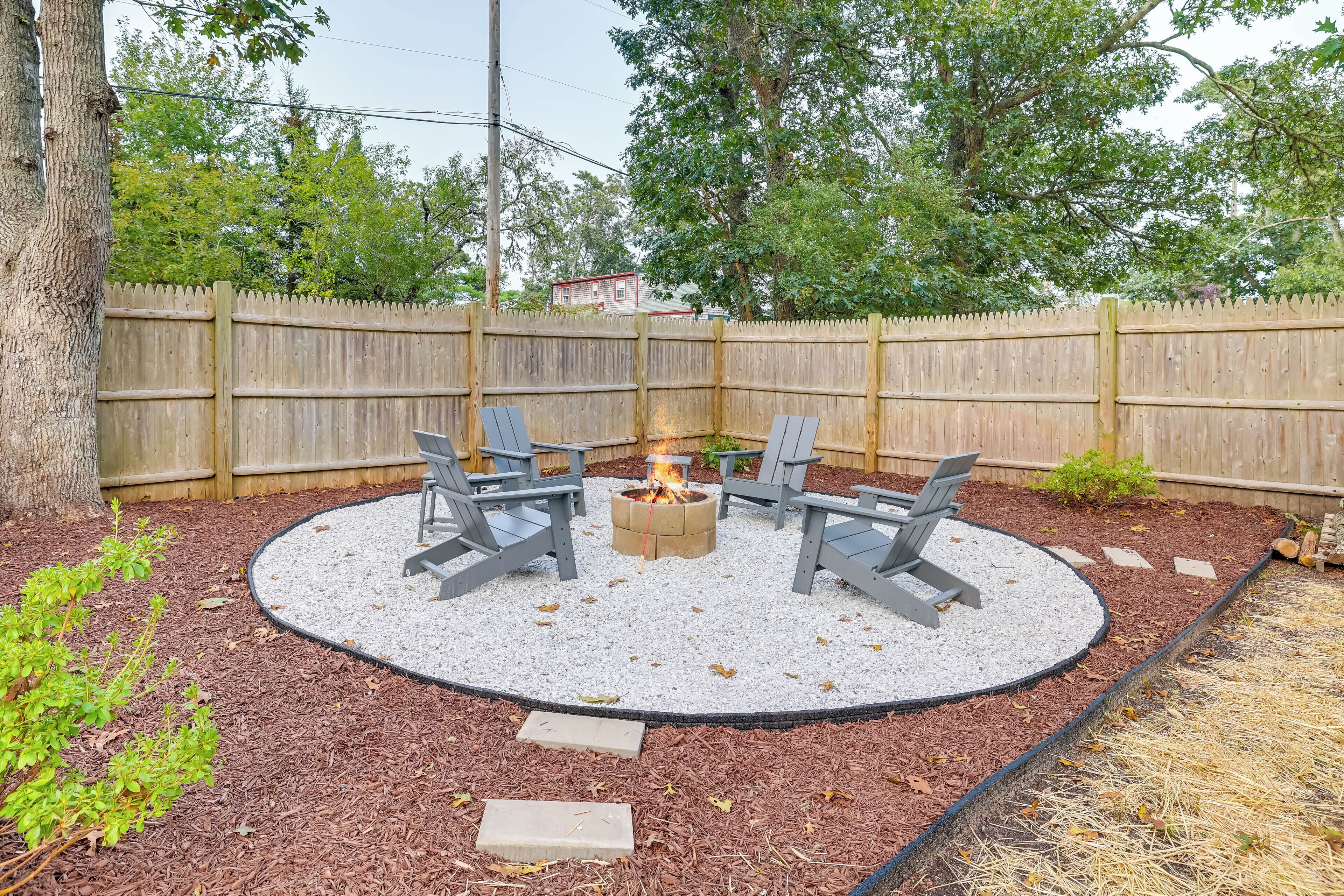 A circular outdoor seating area with four chairs and a central fire pit, surrounded by mulch and gravel.