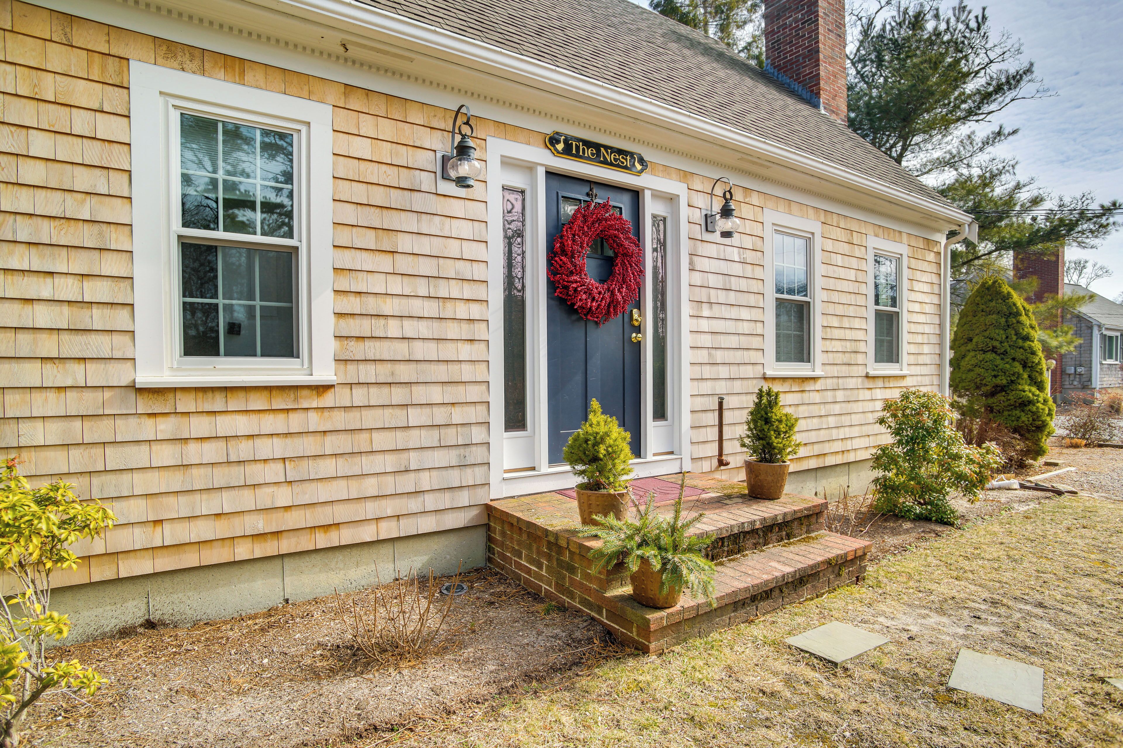 A house with a dark blue front door, a red wreath, and two potted plants on the front steps.