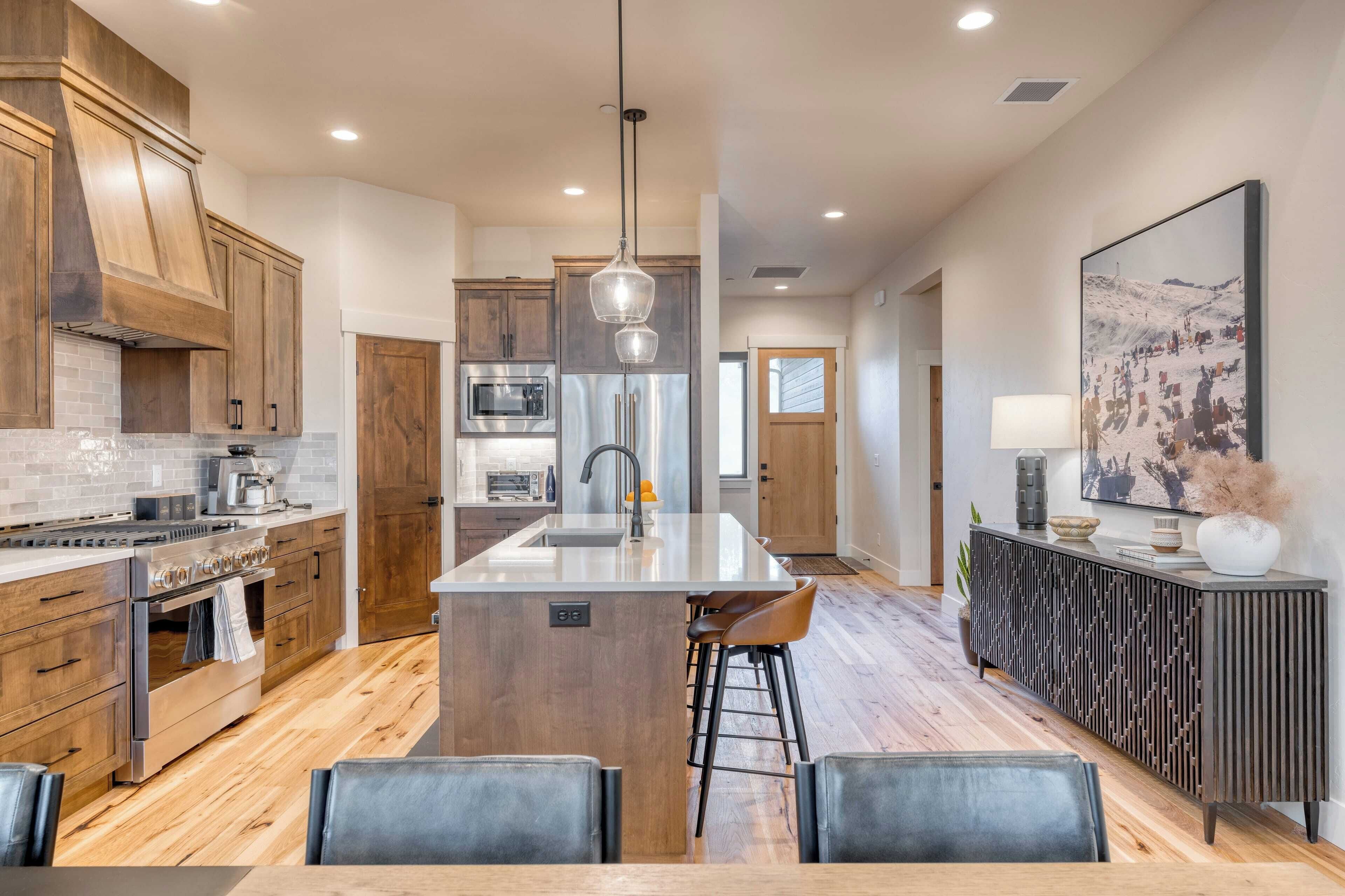 A modern kitchen with wooden cabinets, a central island, and a dining area with bar stools.