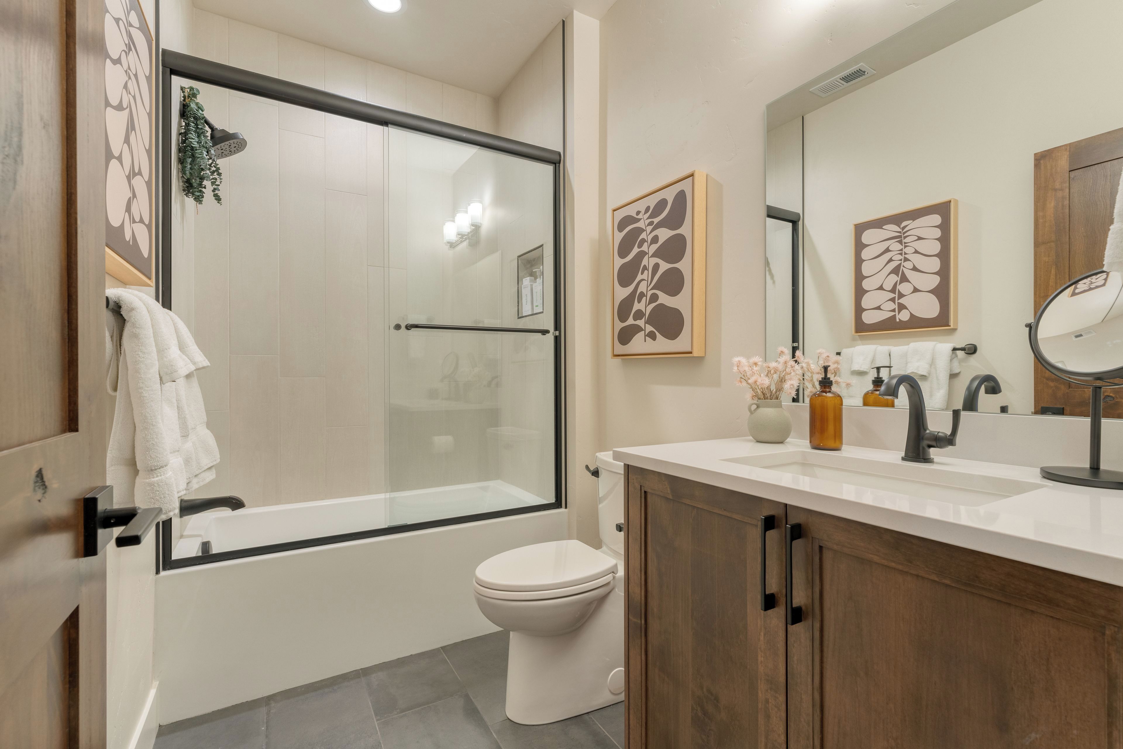 A modern bathroom with a glass shower enclosure, a toilet, a vanity with a mirror, and decorative wall art.