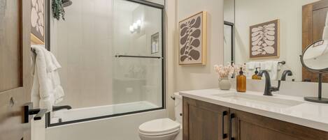 A modern bathroom with a glass shower enclosure, a toilet, a vanity with a mirror, and decorative wall art.