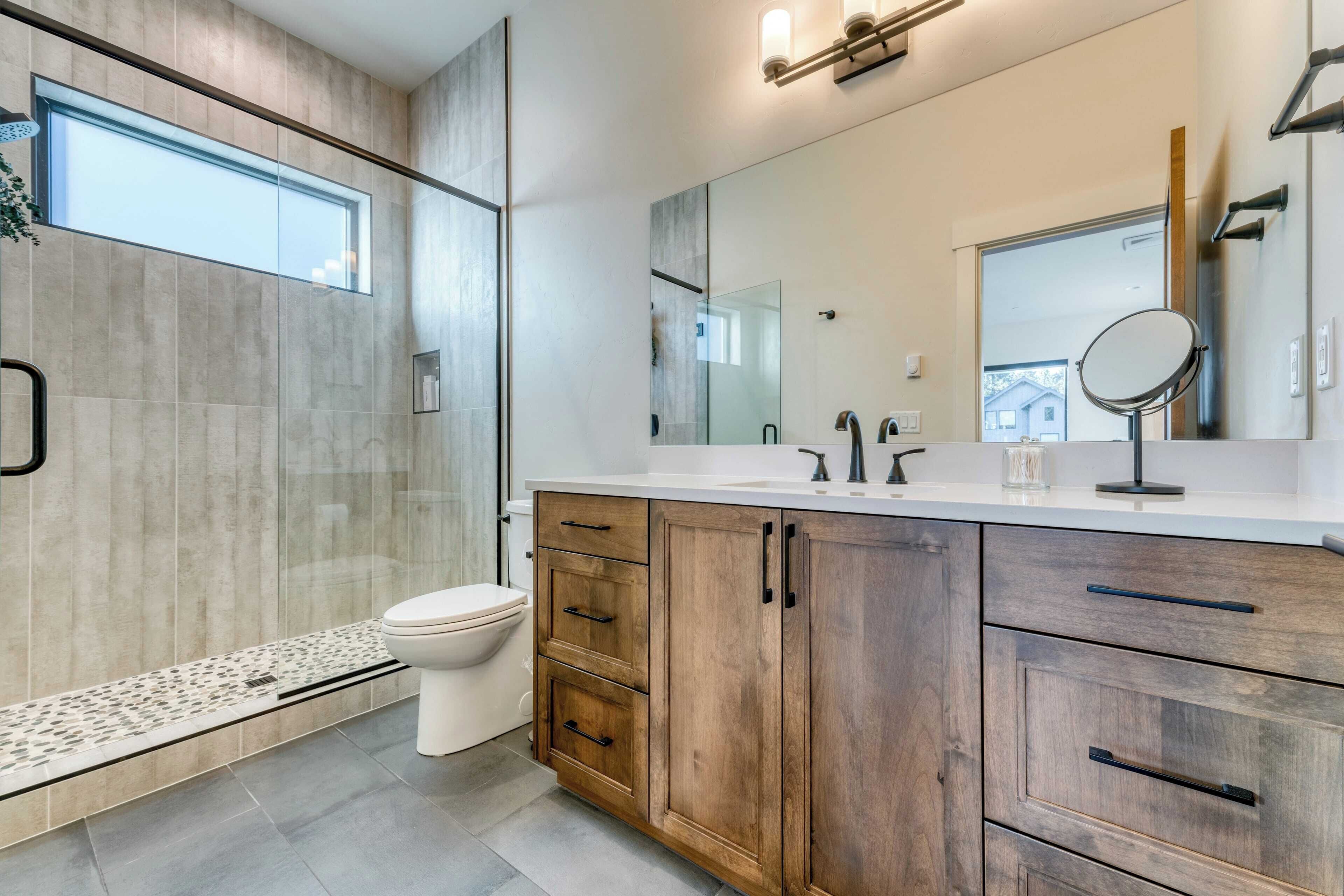 Une salle de bain moderne avec une douche à parois de verre, des toilettes blanches, des meubles en bois et un grand miroir.