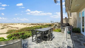 Eine Terrasse mit Tisch und Stühlen, einem Grill und Blick auf den Strand.