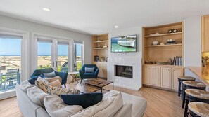 Una sala de estar con sofá, sillones, una mesa de centro, televisor, chimenea y vista a la playa.