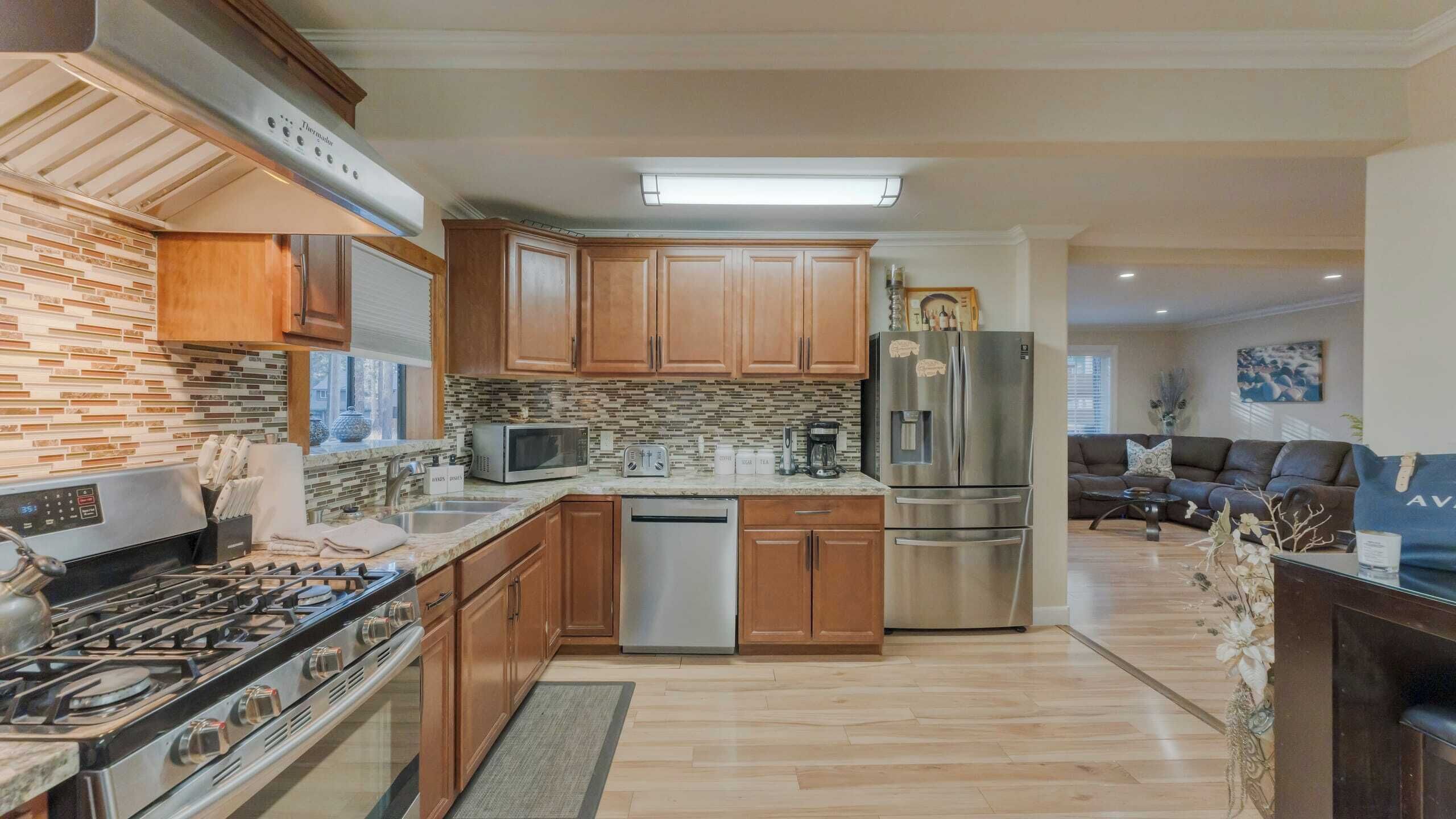 A modern kitchen with wooden cabinets, a stainless steel refrigerator, a microwave, and a gas stove.