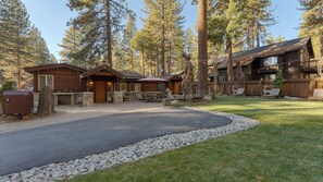 A cabin with a stone patio, outdoor seating, and a view of tall pine trees. - Lake Star by Avantstay Hot Tub, Walk to Beach (Kings Beach)