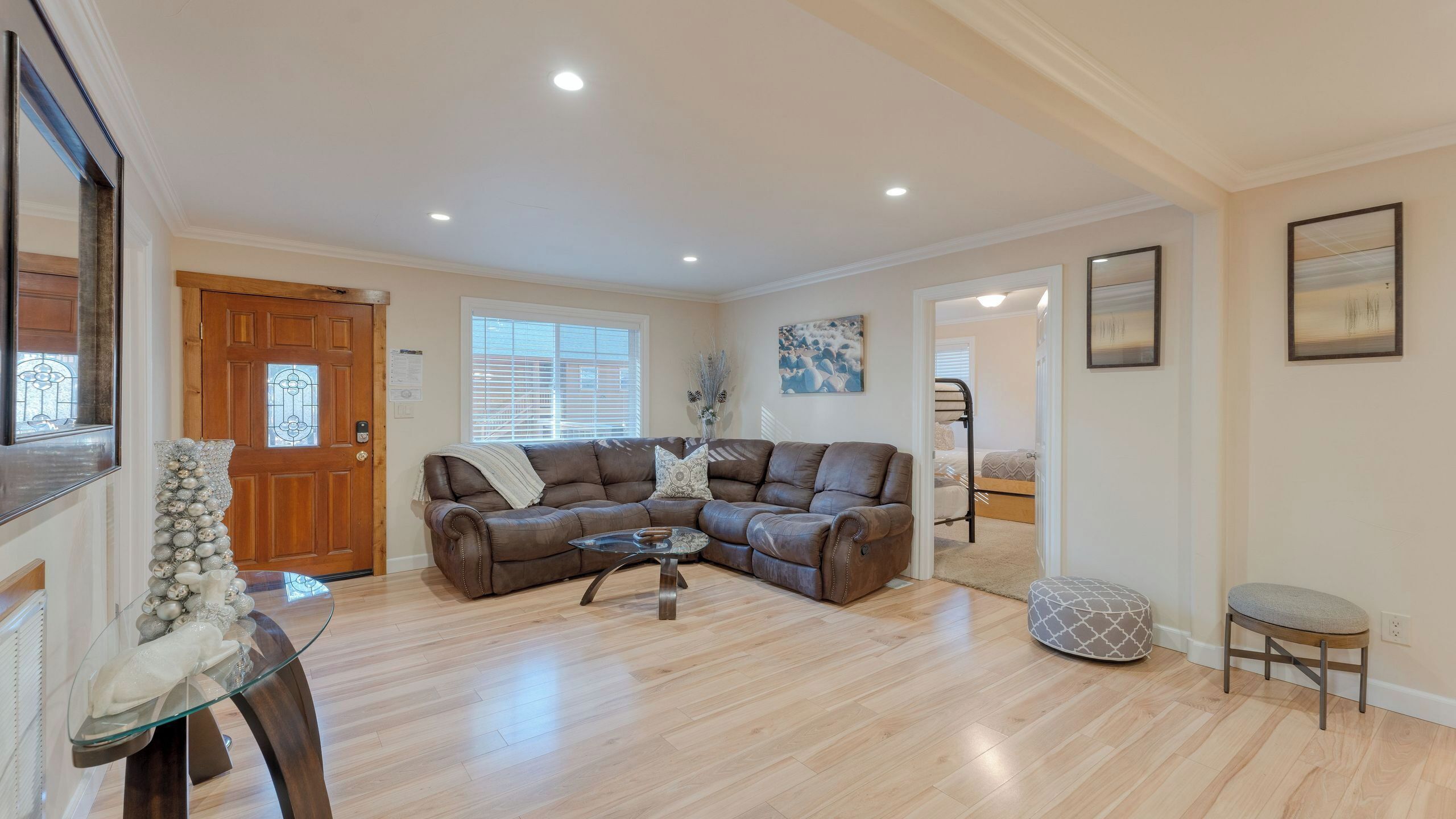 A spacious living room with a brown leather sectional sofa, a glass coffee table, and a wooden floor.