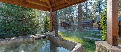 A hot tub under a wooden pergola with a forest backdrop.
