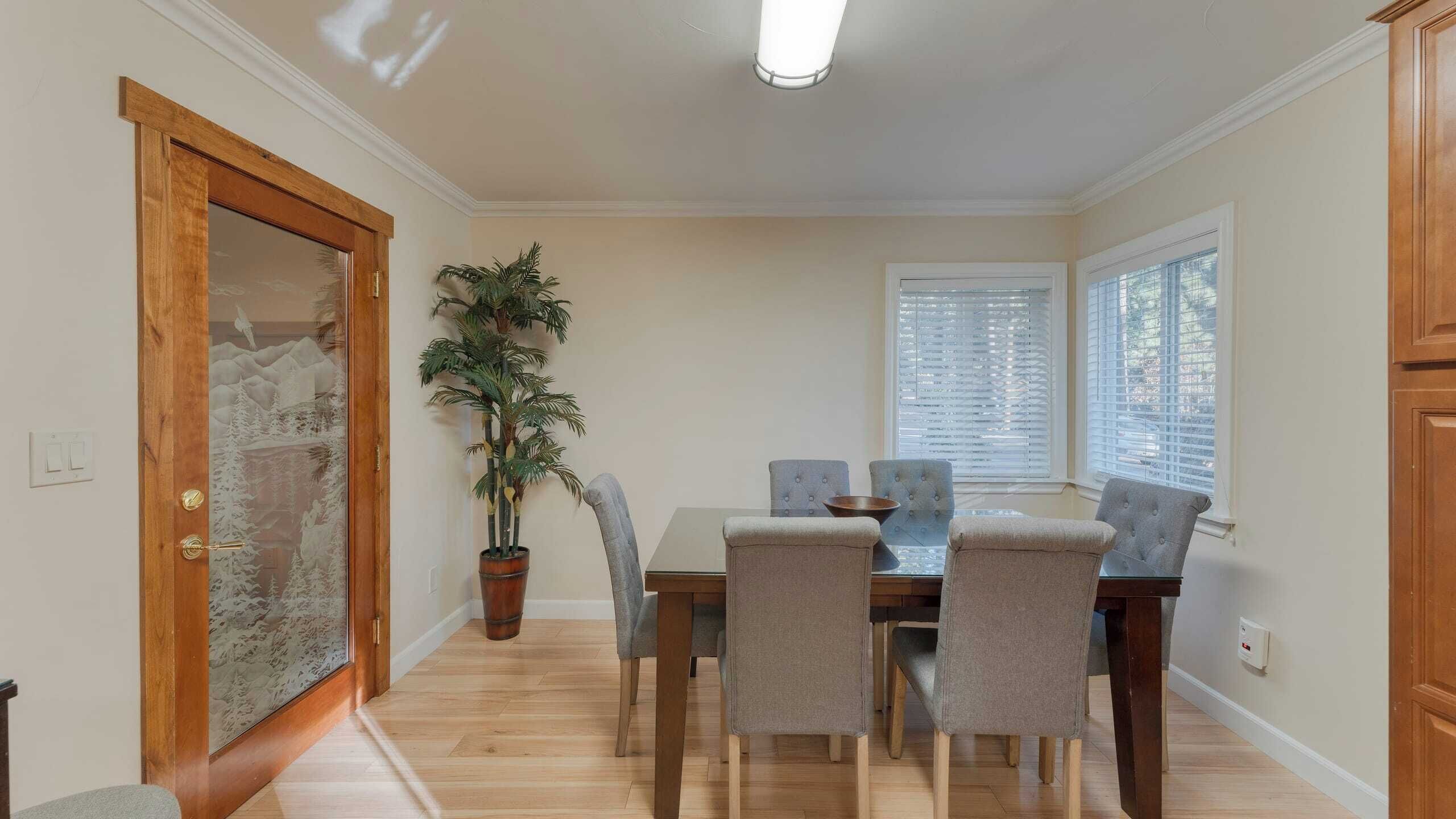 Un coin repas avec une table et des chaises en bois, une plante en pot et une fenêtre avec des stores.