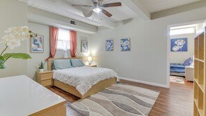 Um quarto com cama, mesas de cabeceira, ventilador de teto e obras de arte nas paredes.