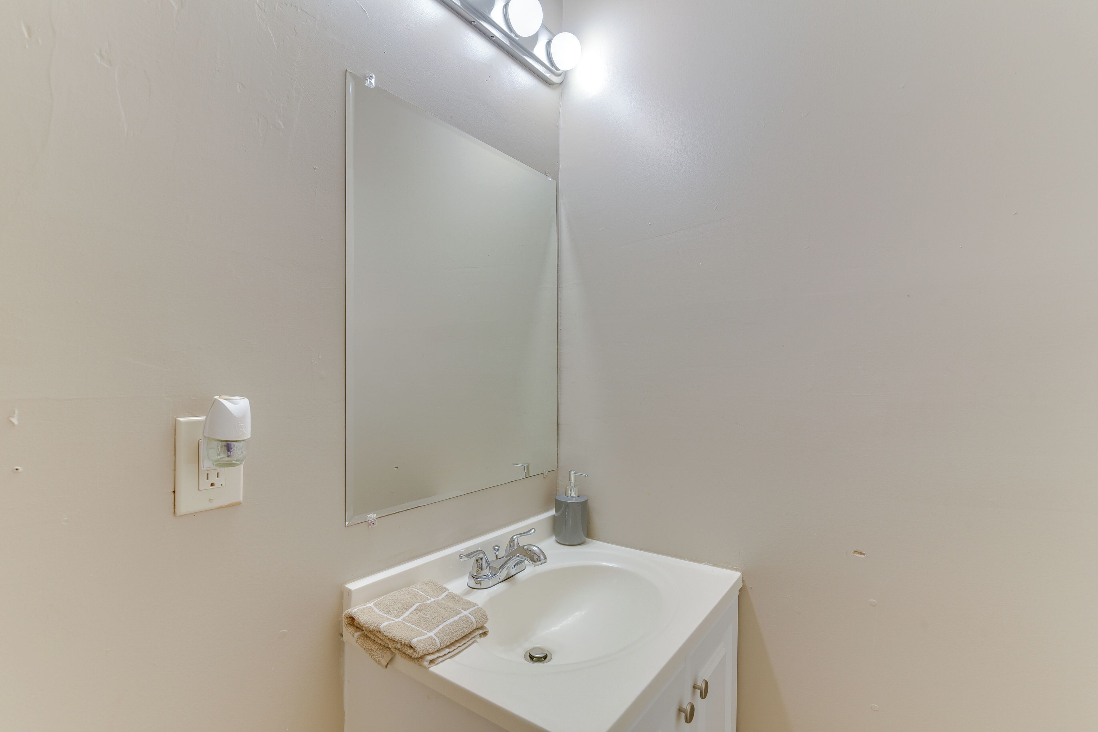 Een badkamer met een wit wastafelmeubel, een spiegel en een lamp boven de spiegel.
