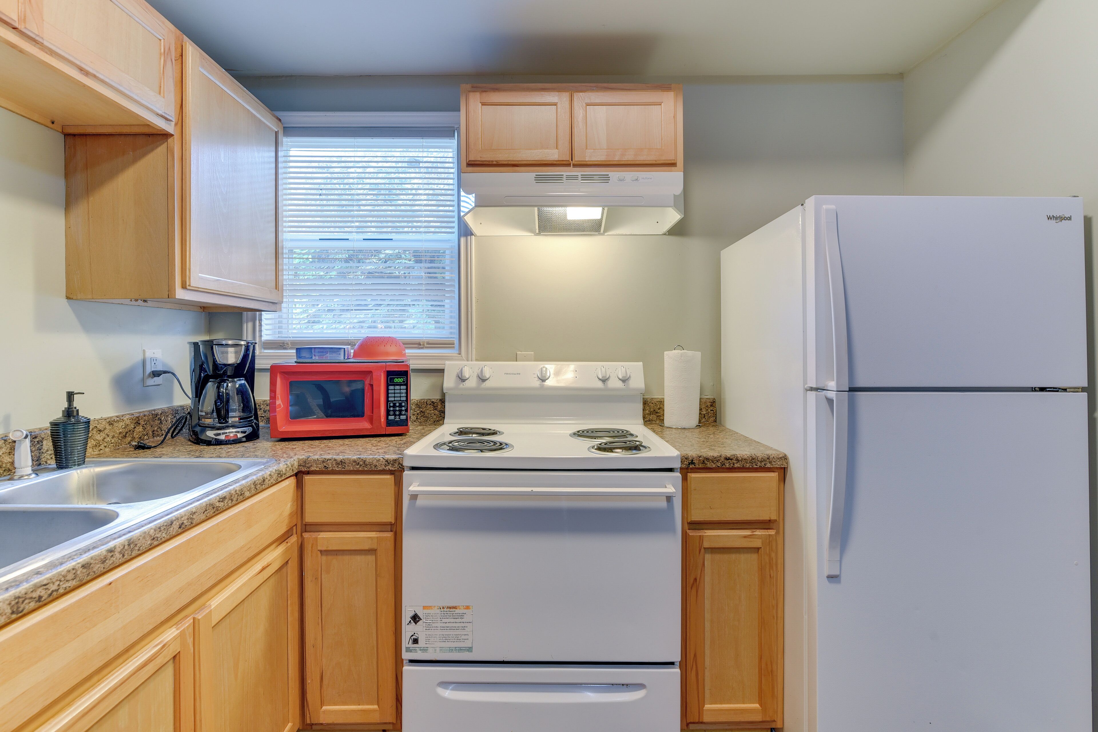 A kitchen with wooden cabinets, a white stove, a microwave, and a refrigerator.