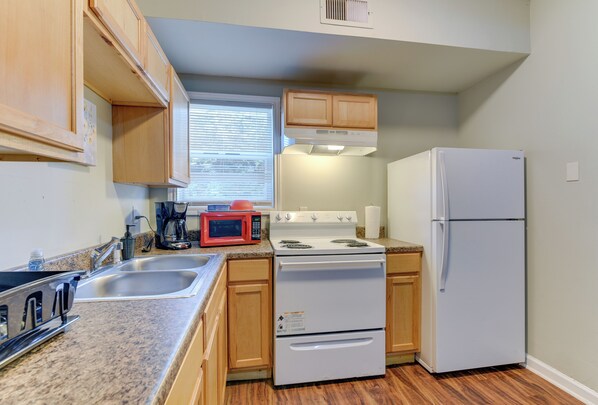 A kitchen with wooden cabinets, a white stove, a refrigerator, and a microwave.