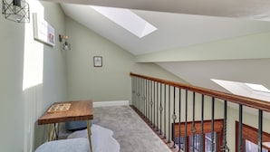 Un escalier avec une main courante en bois et des balustrades en métal, menant à une mezzanine dotée de lucarnes.