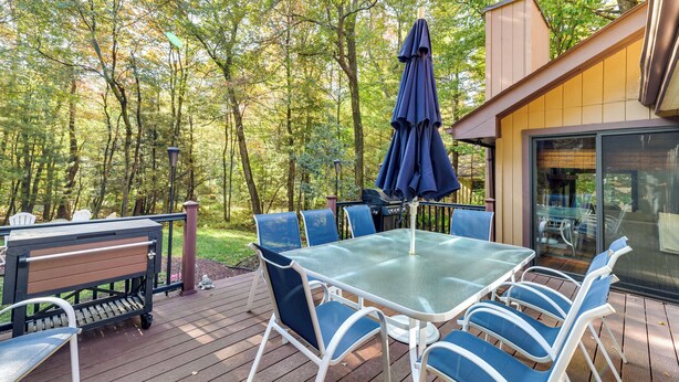 Une terrasse avec une table et des chaises en verre, un barbecue et un parasol.