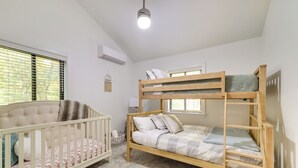 Une chambre à coucher avec un lit superposé, un berceau et une fenêtre avec des stores.