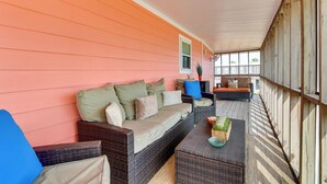 Eine überdachte Veranda mit Korbmöbeln, einer gepolsterten Couch und einem Couchtisch.
