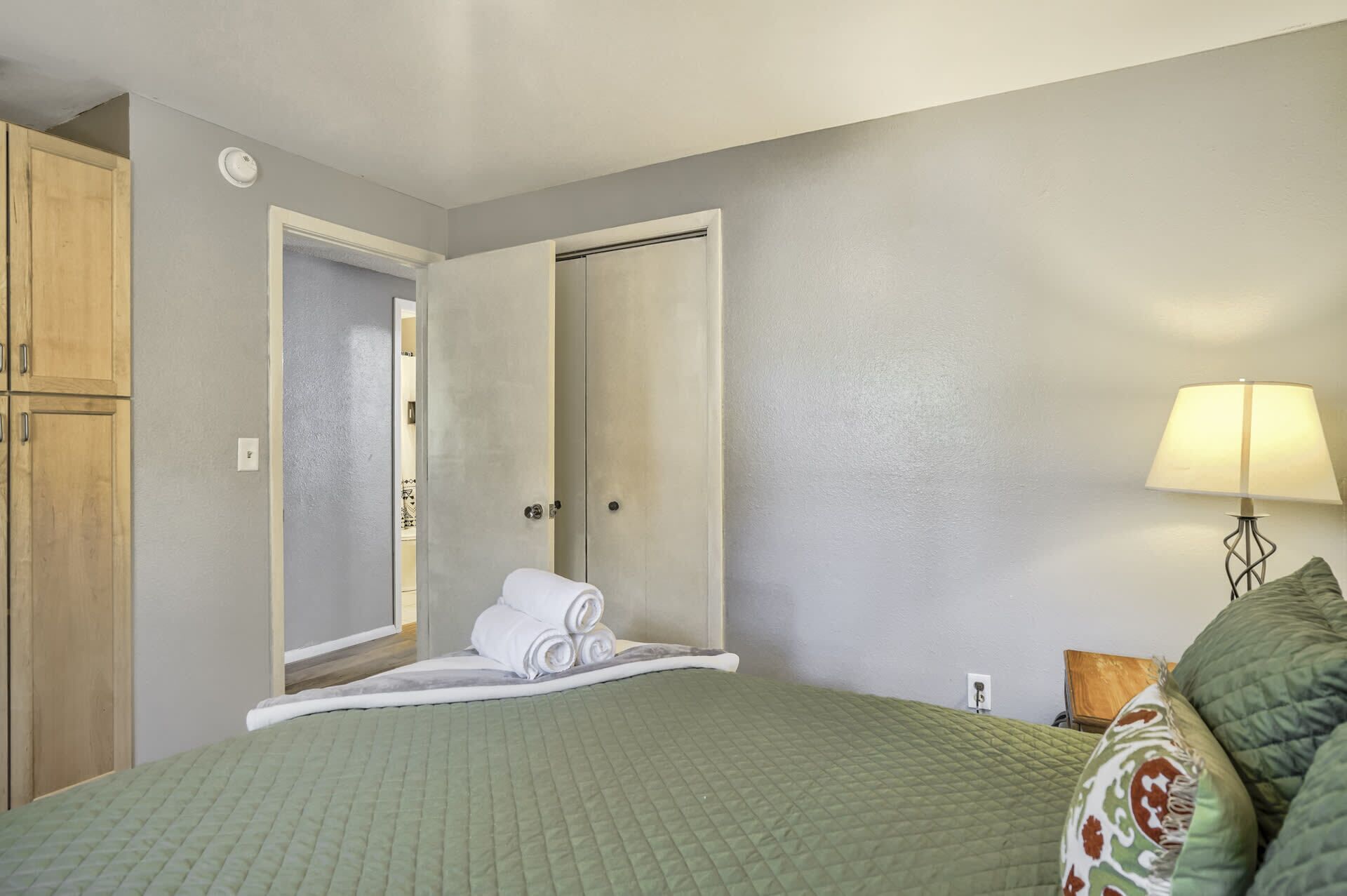 A hotel room with a bed, a nightstand, a lamp, a wardrobe, and a door leading to another room.