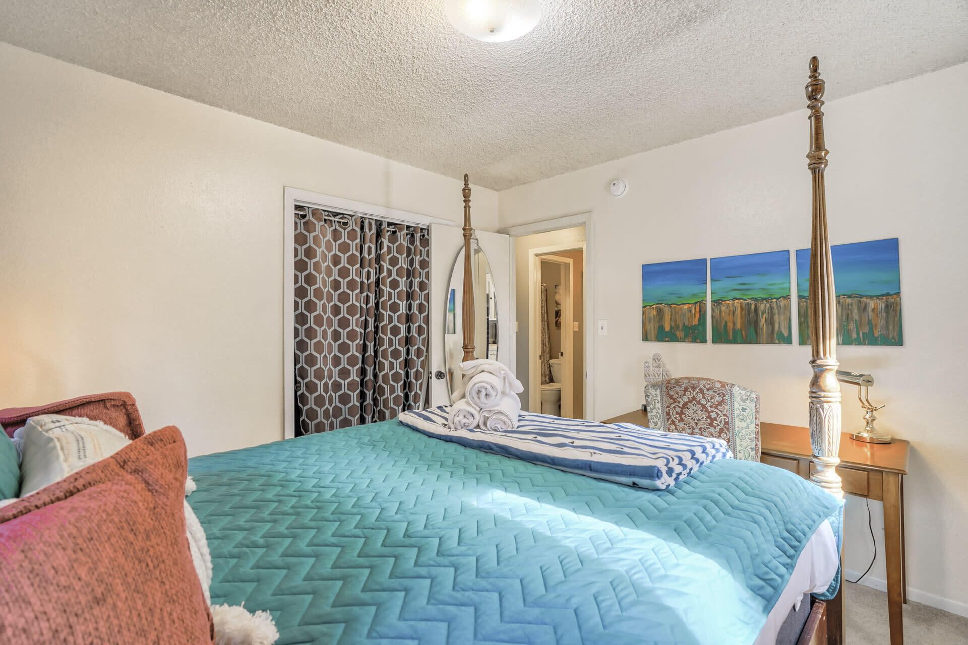 Quarto com cama de dossel, mesa de cabeceira com abajur e vista para o banheiro através de uma porta aberta.