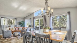 A spacious dining area with a wooden table and chairs, a chandelier, and large windows offering views of trees. - 4bdmountain Getawaydog Friendlyminutes to Pikes Peak & Nature (Woodland Park)