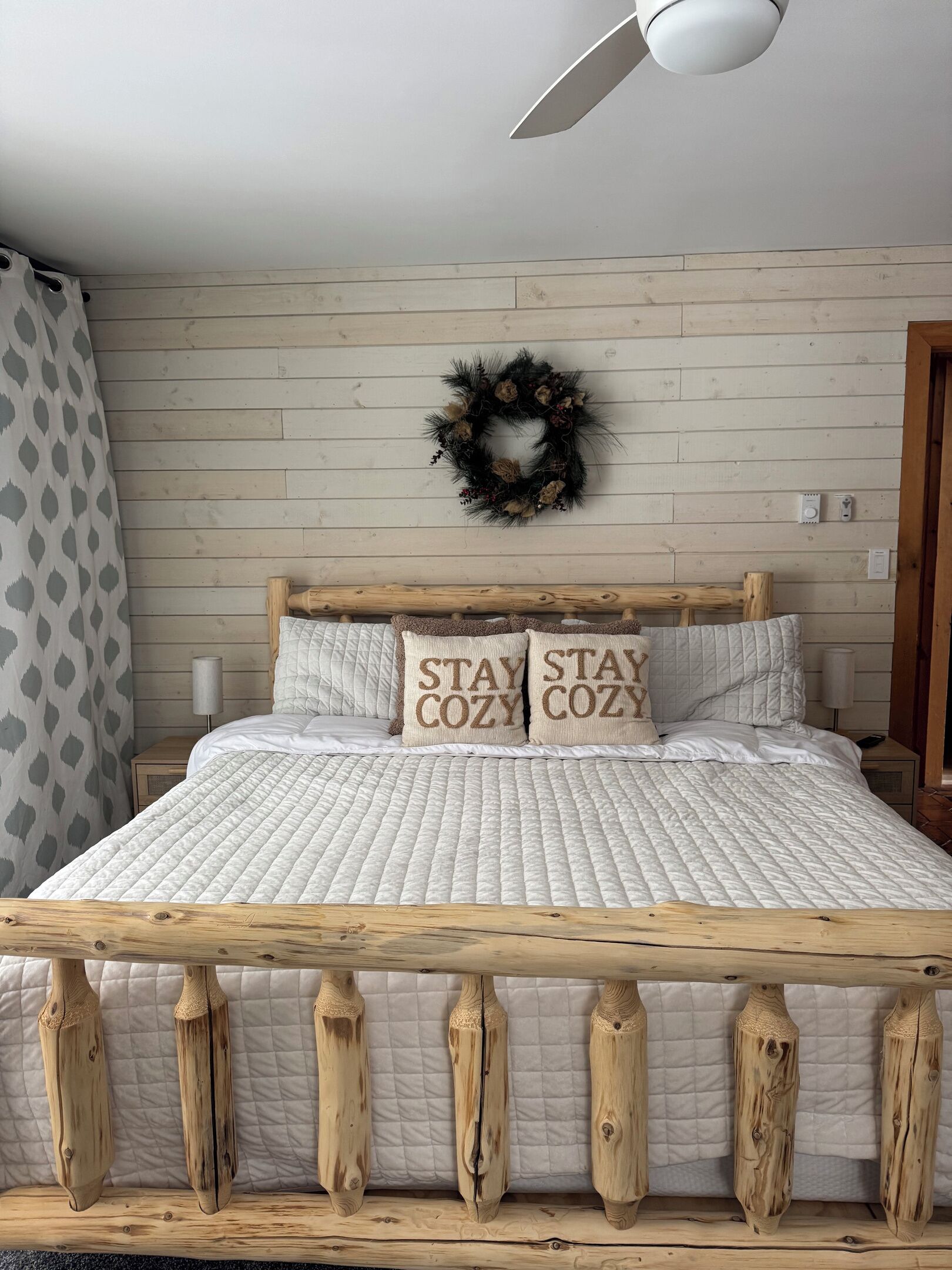 A bed with a wooden frame, a quilted mattress, and two pillows with 'STAY COZY' text.