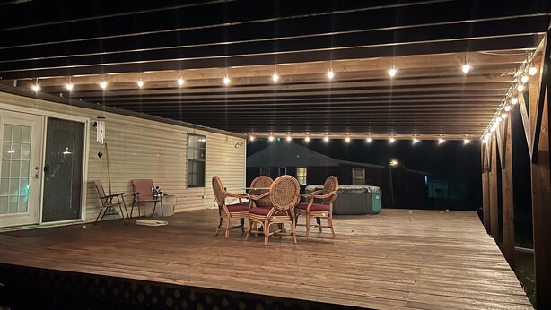 An outdoor deck with a wooden table and chairs, string lights, and a covered area with a view of the backyard. - Vacation rental home Lexington (Lexington)