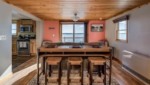 A kitchen with a wooden ceiling, a dining table with stools, and a view of the ocean through a large window. - Black Bay Chalet- Lake front home with magnificent views (Dexter)
