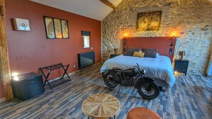 Ein Schlafzimmer mit Steinwand, einem Bett, einem Motorrad und einem runden Holztisch.