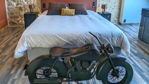 Ein Schlafzimmer mit Steingemäuer, einem Bett, zwei Nachttischen, einem Motorrad und einer Karte an der Wand.