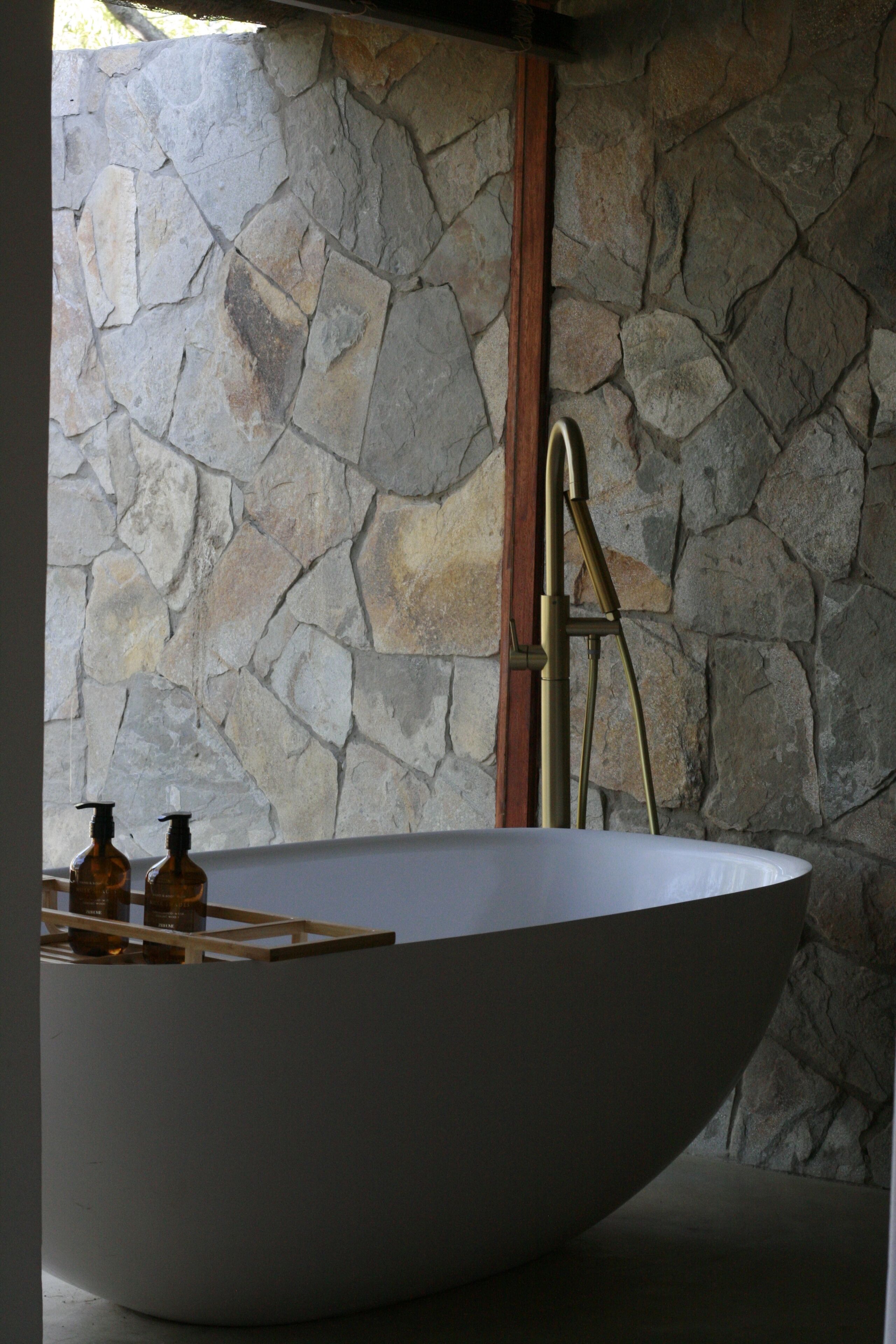 Una bañera grande independiente en un baño con paredes de piedra.