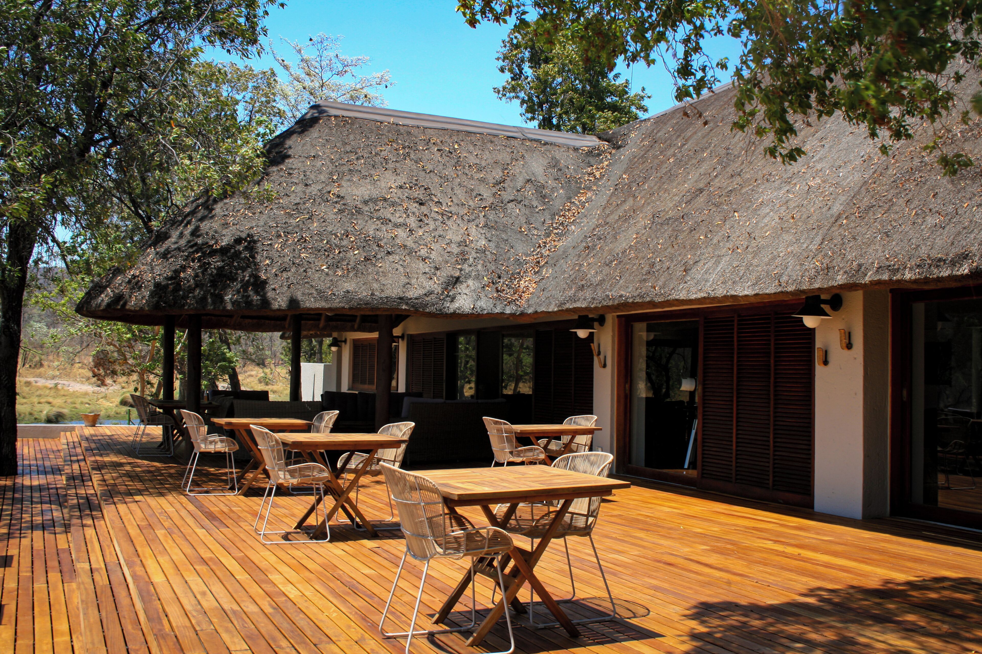 An outdoor dining area with wooden tables and chairs, a thatched roof, and a view of the surrounding landscape.