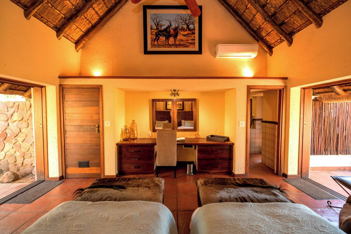 A room with two beds, a desk, and a mirror. There is a stone wall on one side and a wooden door on the other.