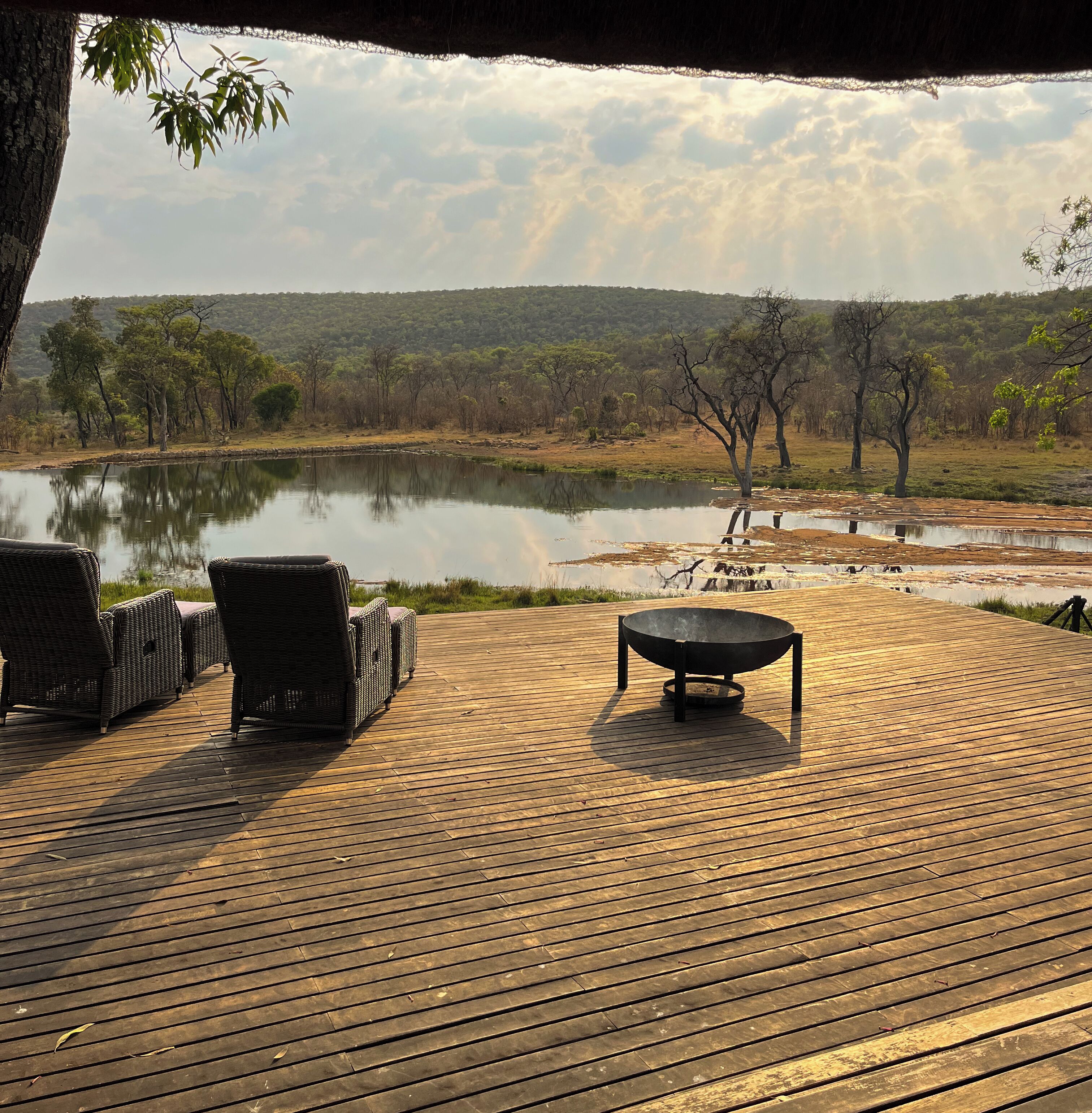 A wooden deck with wicker furniture and a fire pit, overlooking a lake and trees.