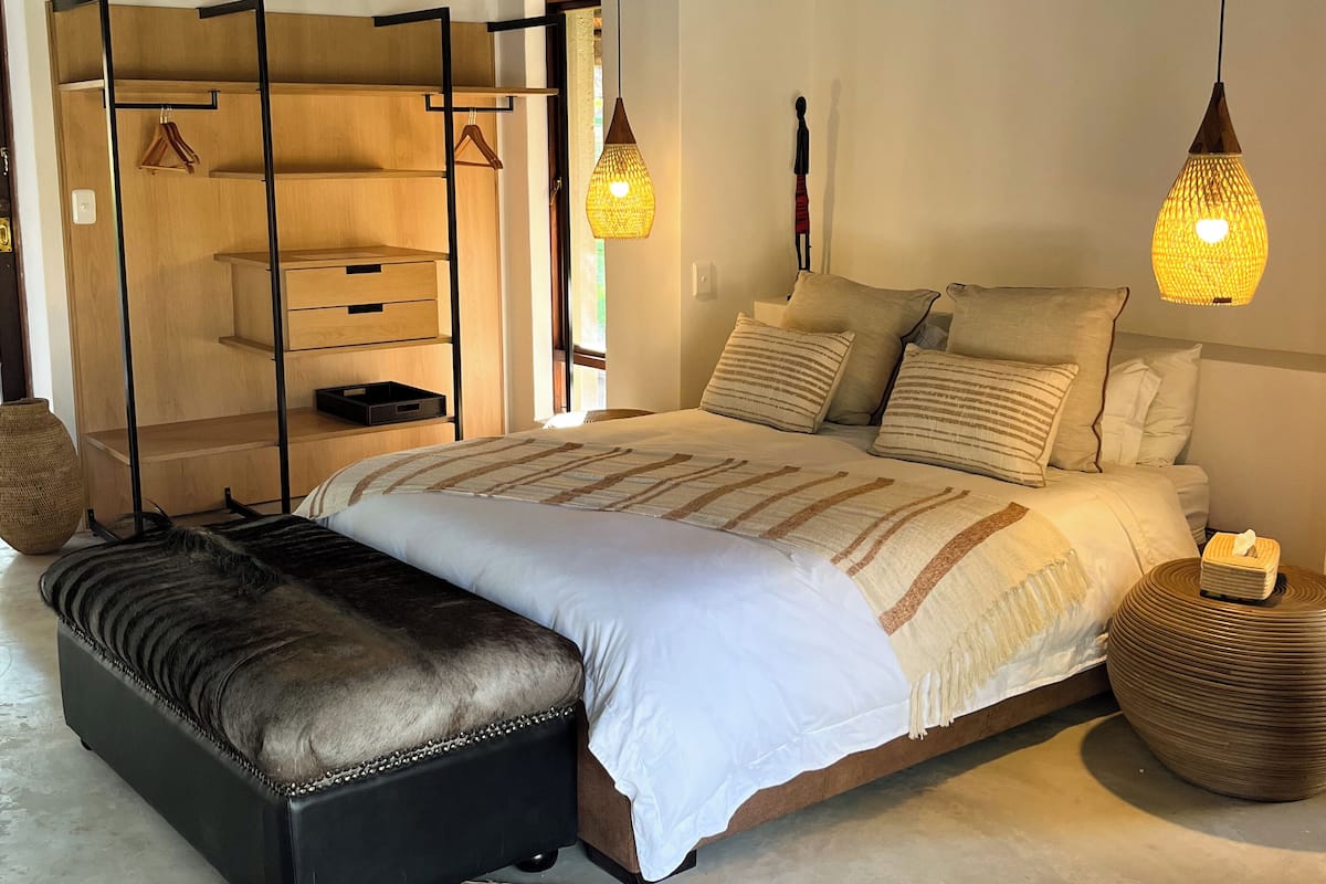 A bedroom with a large bed, a wooden wardrobe, a hanging light fixture, and a ceiling fan.