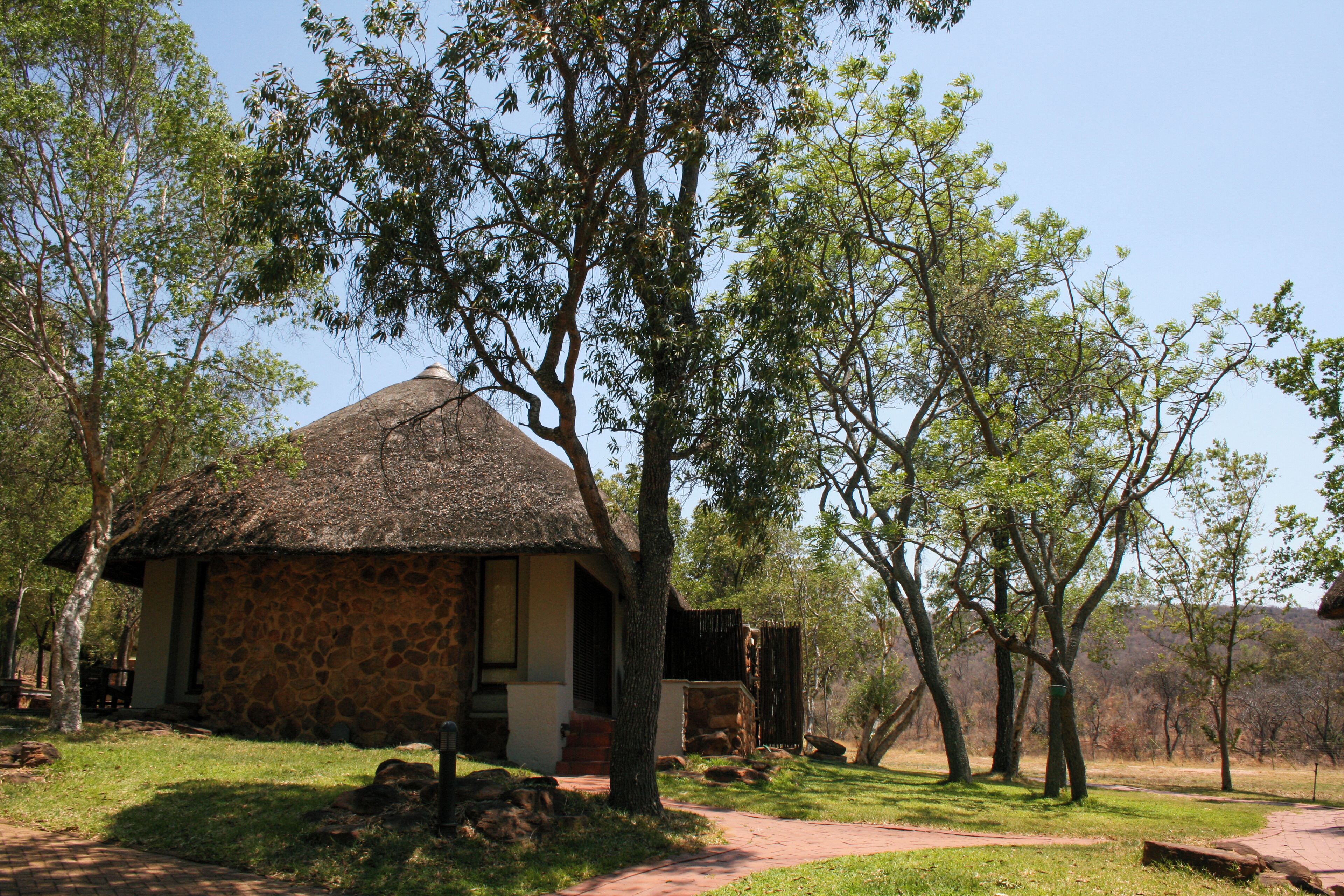 Un bâtiment rustique en pierre, doté d’un toit de chaume, entouré d’une végétation luxuriante et d’arbres.